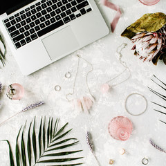 flat lay feminine home office workspace with laptop, proteus flower, necklace, palm branches and accessories. top view