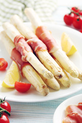 Fresh white asparagus wrapped in jamon on a blue wooden table