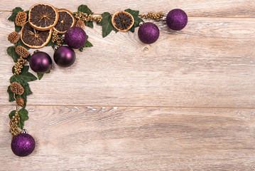 Christmas frame with purple decoration, dry orange and leaves on black wood background with copy space