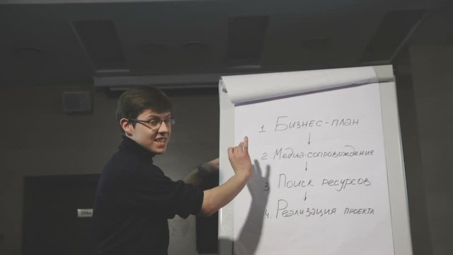 Young man pointing at flipchart while giving presentation to his colleagues