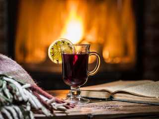 Hot mulled wine and a book on the wooden table. Fireplace with w