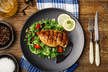 Grilled chicken breast with green salad on a black plate.