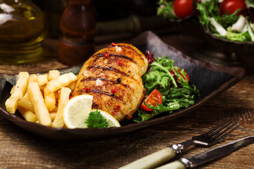grilled chicken breast with green salad and french fries.
