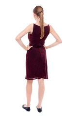 back view of standing young beautiful woman. girl in a burgundy dress sleeveless standing with hands on waist.
