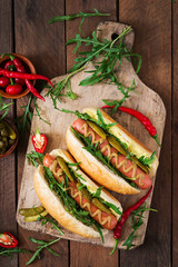 Hot dog with pickles, capers and arugula on wooden background. Top view