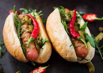 Hot dog with pickles, capers and arugula on wooden background.