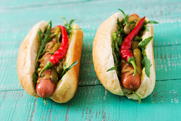 Hot dog with pickles, capers and arugula on wooden background.
