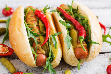 Hot dog with pickles, capers and arugula on wooden background.