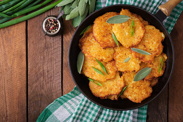 Fried potato pancakes in a frying pan on a wooden table. Top view