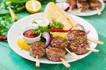 Appetizing kofta kebab (meatballs) with sauce and tortillas tacos on a white plate