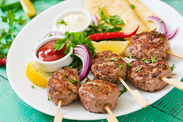 Appetizing kofta kebab (meatballs) with sauce and tortillas tacos on a white plate