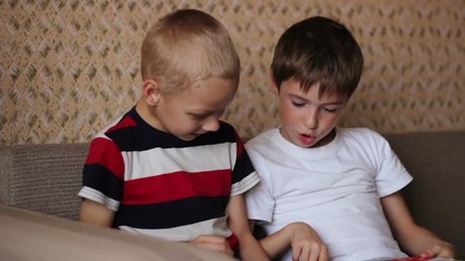 Two boys sitting on a couch and read a book smiling - Powered by Adobe