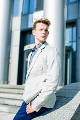 Elegant young handsome man wearing  white jacket and jeans near building