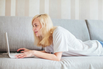 woman in pajamas with laptop lying on the sofa