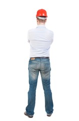 Backview of an engineer in construction helmet stands. Standing young guy. Rear view people collection.  backside view of person.  Isolated over white background. Engineer crossed his arms and watches