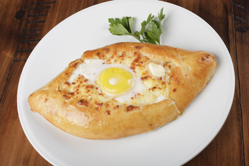 Khachapuri - traditional georgian pie with potatoes and cheese. Cake on a white plate. Wooden background