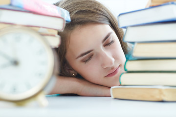 Tired female student at workplace in classroom taking nap near a pile of books. Student in despair caused by exam deadline concept