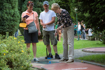 Drei Generationen Familie hat Spass am Minigolf spielen. Die Großmutter richtet den Schläger am...