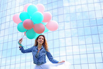 Beautiful young woman with colorful balloons against glass-facade building