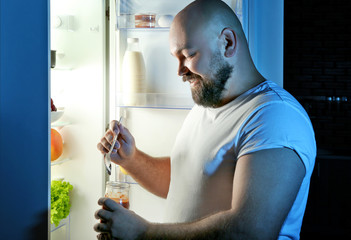Man eating at night next to refrigerator
