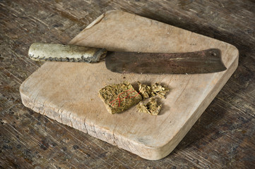 dry hashish piece on old chopping block with old knife