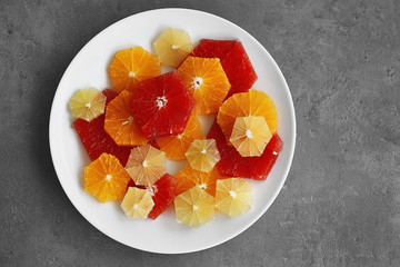 Plate with different citrus slices on grey background