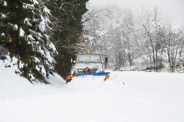 Snow plough making its way through the snowy country road, clearing it of snow after blizzard. Professional winter services, road conditions in winter concept. .