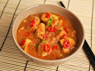 Tasty chicken curry in bowl and chopsticks on bamboo mat