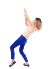back view of standing girl pulling a rope from the top or cling to something. Isolated over white background. The blonde in a pink shirt pulling the rope from above.