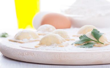 Homemade ravioli on a round wooden board and egg flour oil parsley