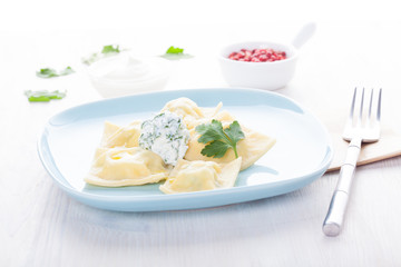 Homemade ravioli on a blue plate with sauce and seasonings