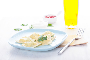 Homemade ravioli on a blue plate with sauce and seasonings