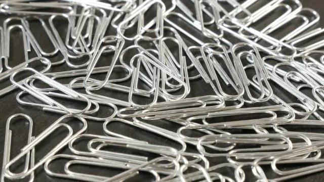 Lot of metal paper clips on office wooden table close-up slow tilt 4K 2160p 30fps UltraHD footage - Steel wire paperclips with looped shape 4K 3840X2160 UHD tilting video 