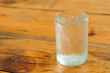 Glass water with drops on glass places on wooden table.