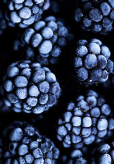 Close up view on frozen Blackberry fruits, on a black stone table. Food background. Dark photo style.