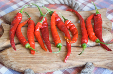 Eleven fresh red chili peppers on a handmade wooden board under a daylight - 120076763