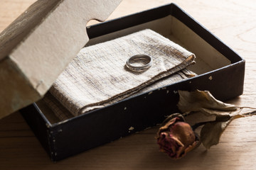 still life photography : old silver ring and old handkerchief in old paper box with dry rose in remembrance of love concept