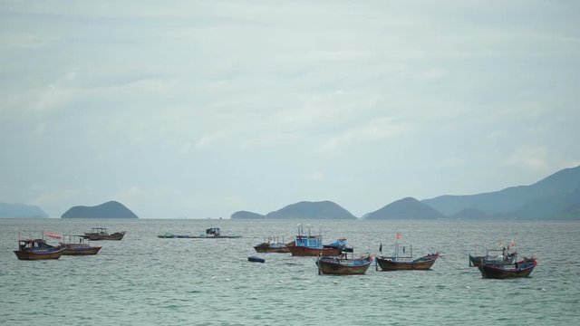 Group of fishing boats is shaking on water at the local vietnamese river. Summer windy cloudy weather.