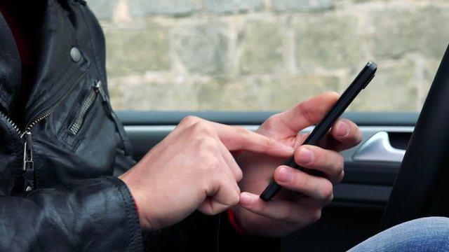 man sits in the modern car and works on smartphone - closeup hands