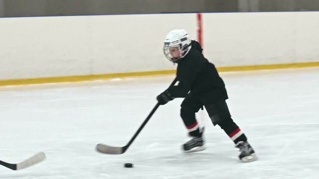 Slow motion tracking shot of novice ice hockey player dribbling puck and failing to score goal as defenseman from opposite team leg checking him