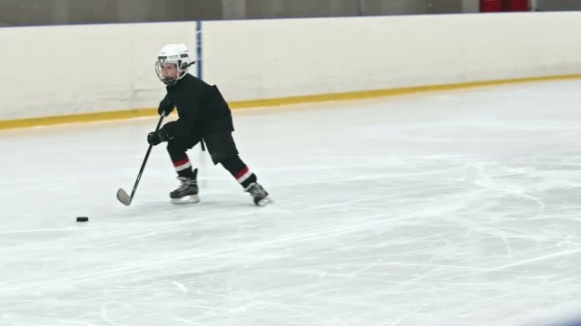 Slow motion tracking of little ice hockey player practicing dribbling puck during drill in indoors ice rink