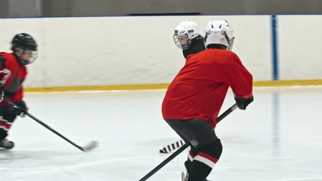 Slow motion tracking of little player from minor ice hockey league dribbling and shielding puck from opposite teams defense and then failing to score goal during practice in ice rink 