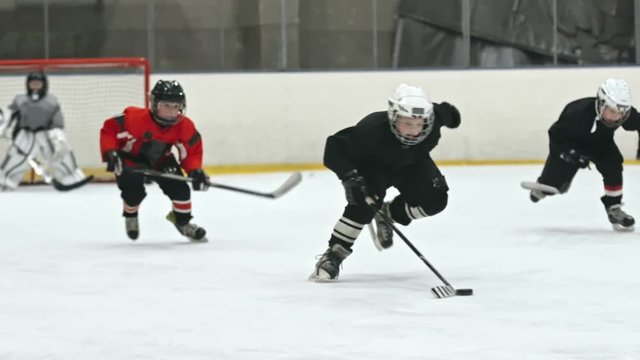 Minor league hockey players speeding on ice and trying to catch up with little forward confidently dribbling puck towards opposite end of ice rink
