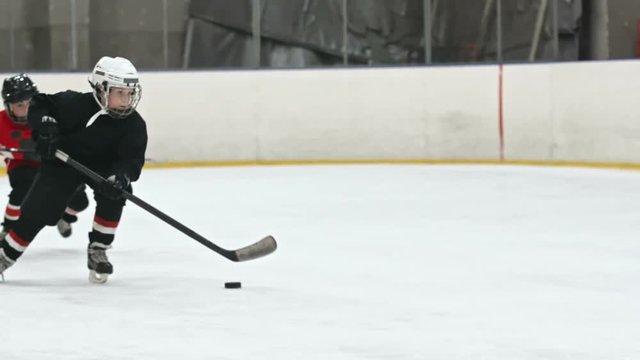 Slow motion tracking of novice ice hockey forward dribbling puck towards opposite teams net 