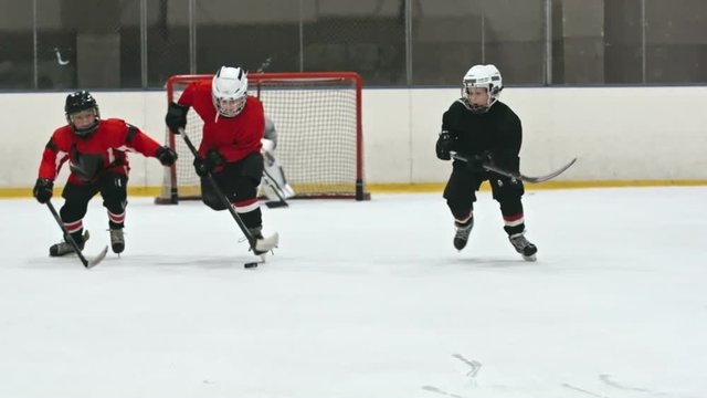 Lockdown shot of little ice hockey players speeding on ice towards camera and desperately fighting for puck, then colliding and falling down in slow motion