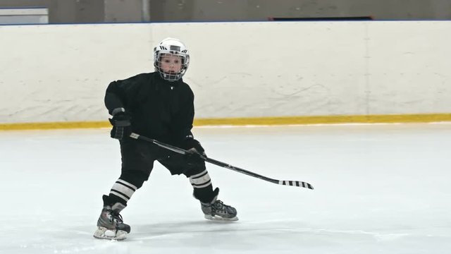 Slow motion tracking of little forward player hitting puck and dribbling while novice defenseman from opposite team body checking him on practice in indoors ice rink