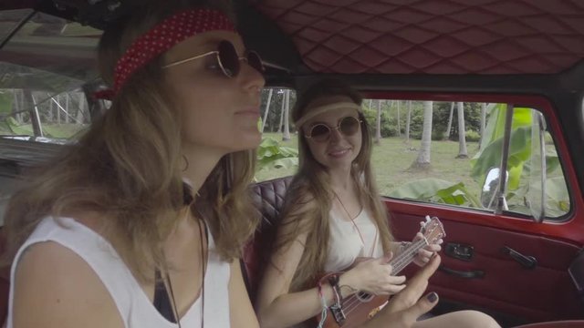 Hippie Girls Have Fun Playing Hawaiian Guitar in a Cabin of Minivan. Slow Motion