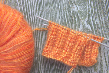 Fototapeta na wymiar Knitting orange mohair wool ball and knitting needles on the old wooden rustic background