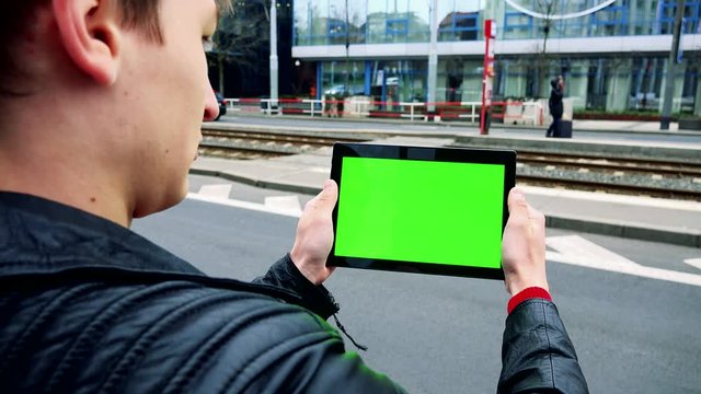 young man works on tablet on urban street in city - green screen 