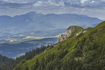 Scenic alpine landscape with green slope and Ciucas Mountain range at  the horizon as seen from Piatra Mare Massif, Romania.